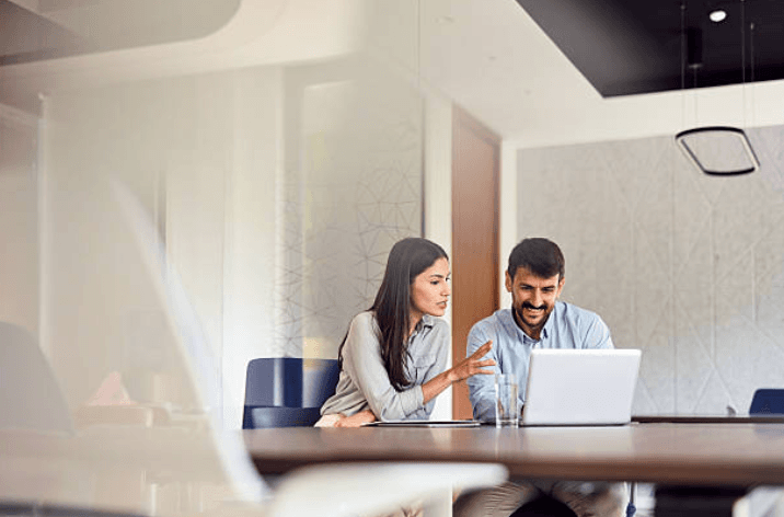 Two professionals collaborating at a laptop in a modern office conference room